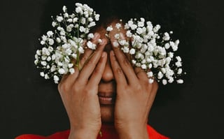 A person covering their face with their hands while hold babies' breath flowers.